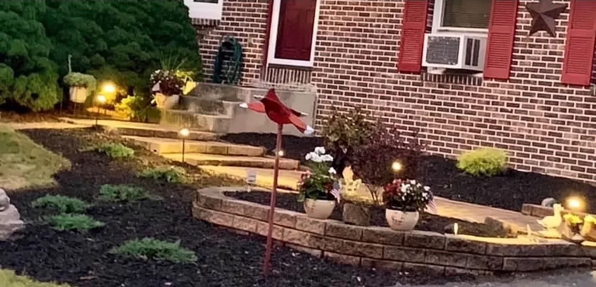 After: fresh mulch beds, a low block wall and path lighting at the front of the same house