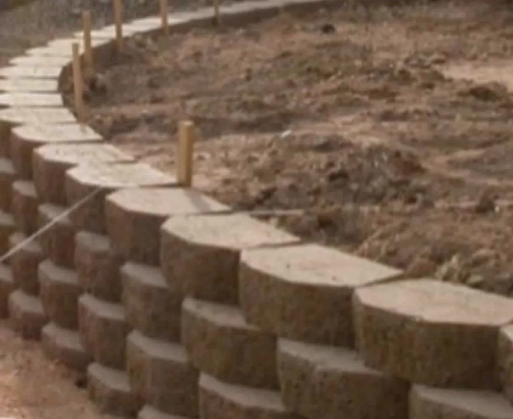 Curved block retaining wall under construction with stakes and bare soil